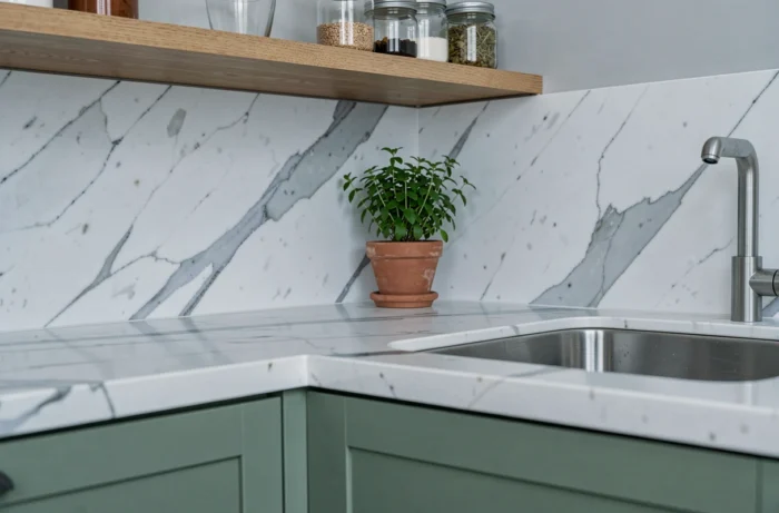 Détail d'un coin cuisine rénovée de 10m2 avec meuble vert sauge, étagère en chêne et plan de travail en marbre blanc, style épuré